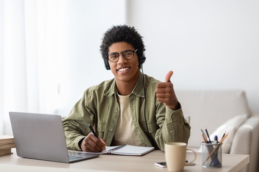 Iloinen nuori mies kirjoittaa ja näyttää peukkua